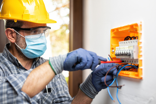 electrician,worker,at,work,on,an,electrical,panel,protected,by